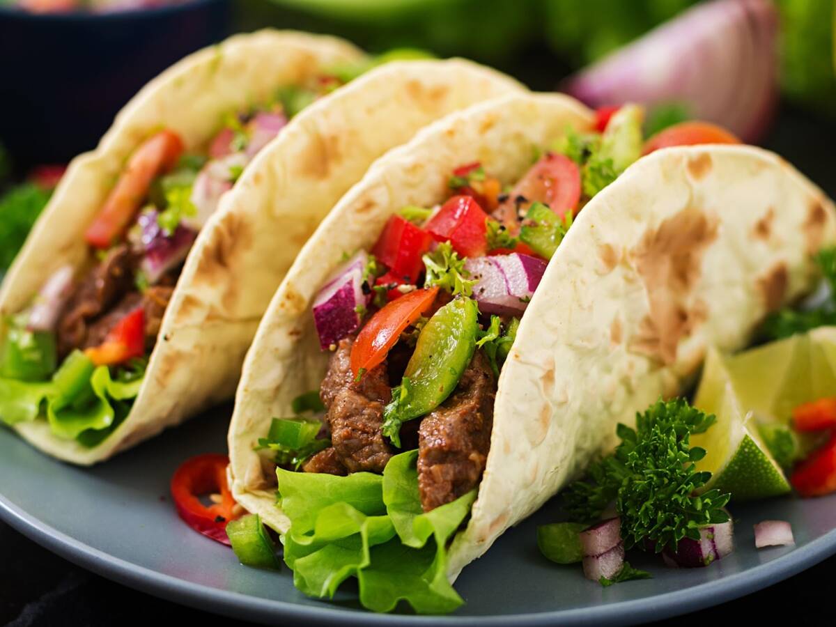 Tacos garnis de coriandre fraîche et d'oignon, avec des quartiers de citron vert