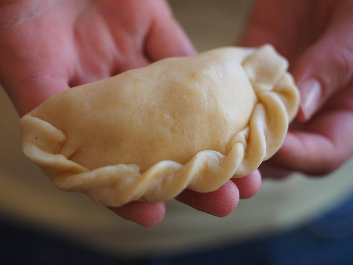 Mains qui plissent le bord d'un ravioli farci sur un plan de travail fariné
