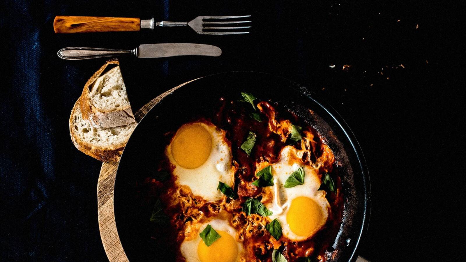 Poêle de sauce tomate aux poivrons dans laquelle cuisent des œufs, parsemée d'herbes fraîches