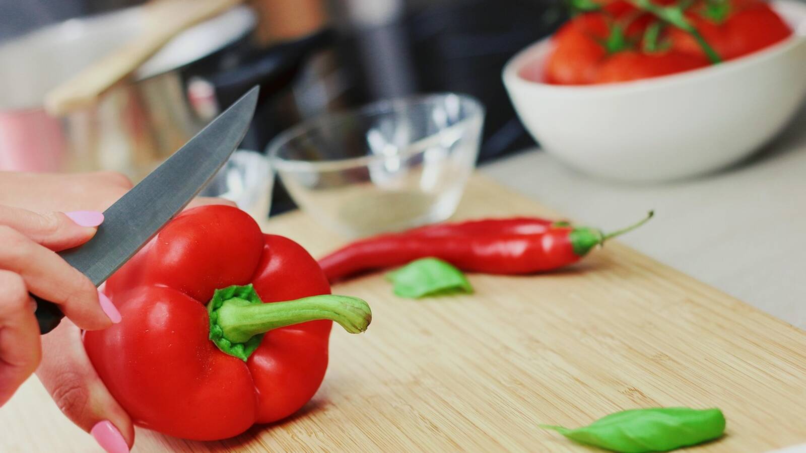 Mains qui coupent des poivrons rouges et un oignon sur une planche